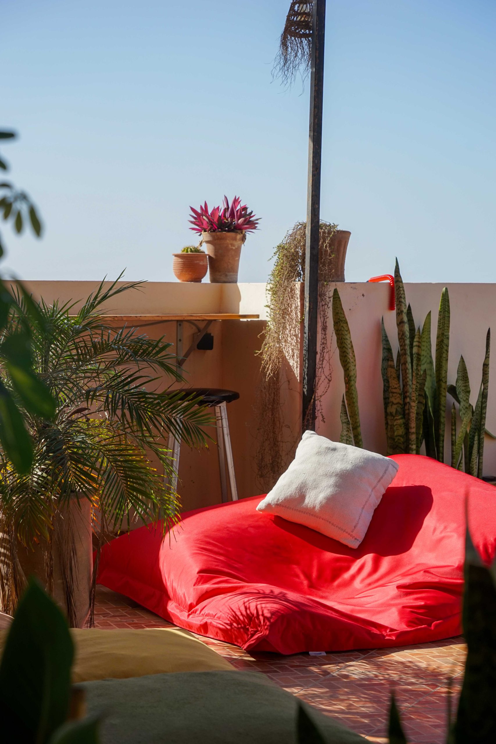 Rooftop lounge with a red bean bag and lush plants at Les Terrasses, perfect for yoga and sunset relaxation in Tamraght.